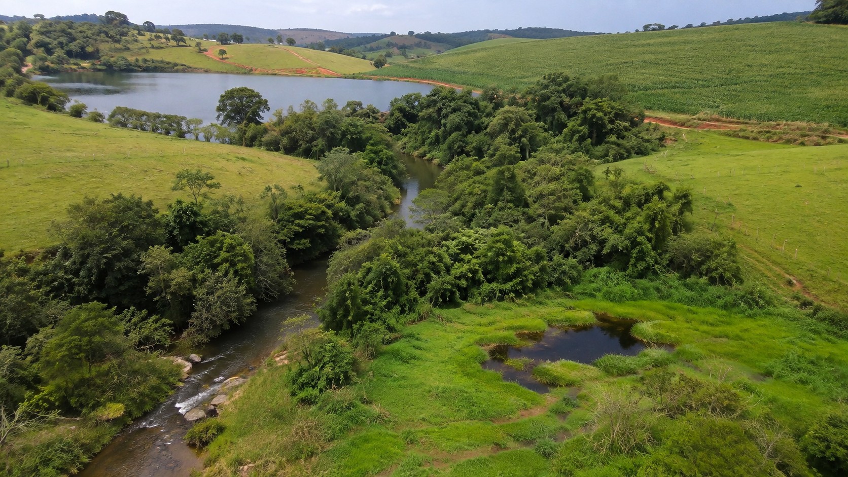 Curso d'água com vegetação à margem, um açude adiante e uma área alagada na lateral. Típica de necessidade de autorização para qualquer tipo de autorização ambiental.